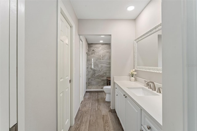 bathroom with tiled shower, wood-type flooring, vanity, and toilet