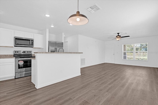 kitchen featuring stainless steel appliances, a center island with sink, white cabinets, and decorative light fixtures