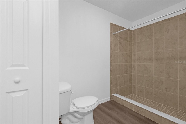 bathroom with wood-type flooring, tiled shower, and toilet