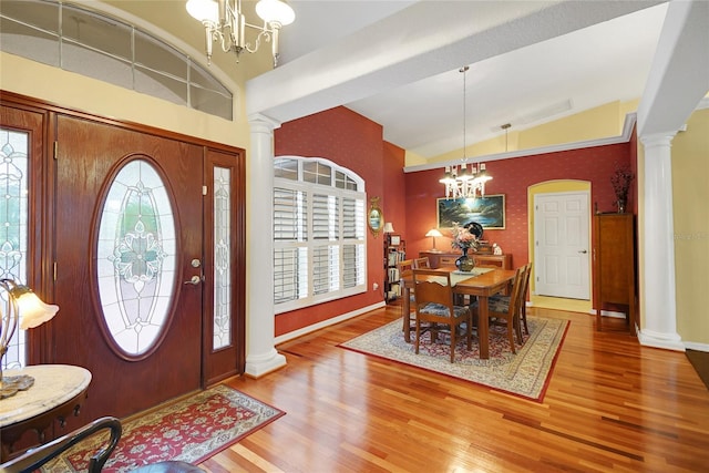 foyer featuring hardwood / wood-style floors, vaulted ceiling, decorative columns, and a chandelier