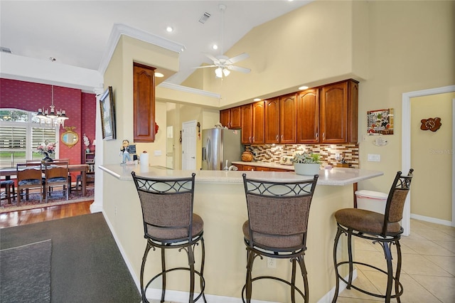 kitchen with kitchen peninsula, stainless steel fridge, ceiling fan with notable chandelier, hanging light fixtures, and light tile patterned flooring