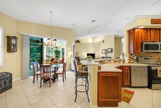 kitchen with appliances with stainless steel finishes, backsplash, light tile patterned floors, pendant lighting, and lofted ceiling