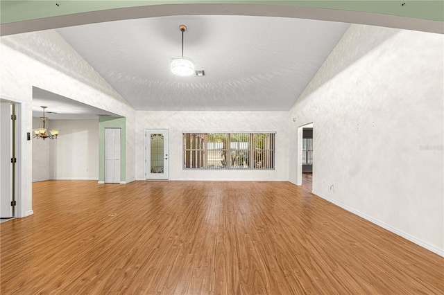 unfurnished living room with hardwood / wood-style floors, high vaulted ceiling, and a notable chandelier