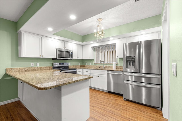 kitchen featuring hanging light fixtures, stainless steel appliances, kitchen peninsula, light hardwood / wood-style floors, and white cabinets