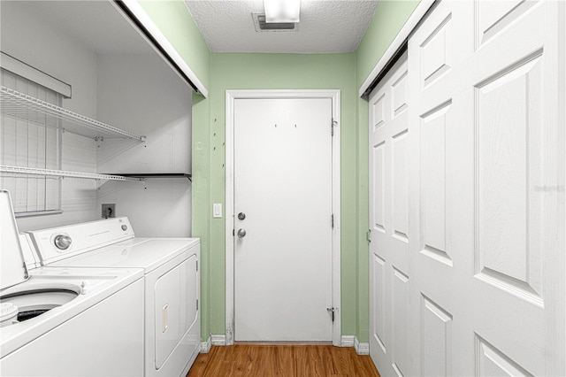 washroom with a textured ceiling, light hardwood / wood-style floors, and washing machine and clothes dryer