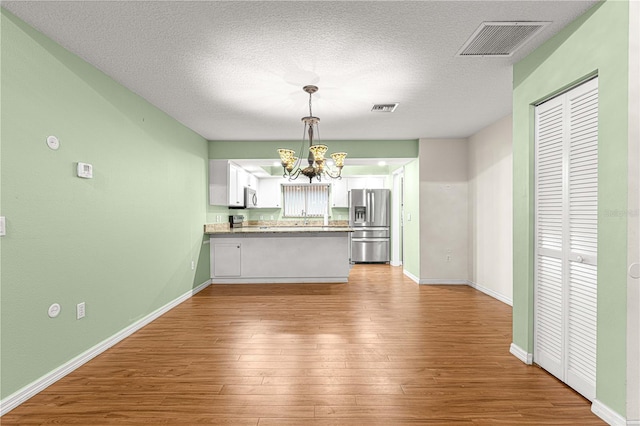 kitchen featuring white cabinets, light wood-type flooring, a textured ceiling, decorative light fixtures, and stainless steel fridge with ice dispenser