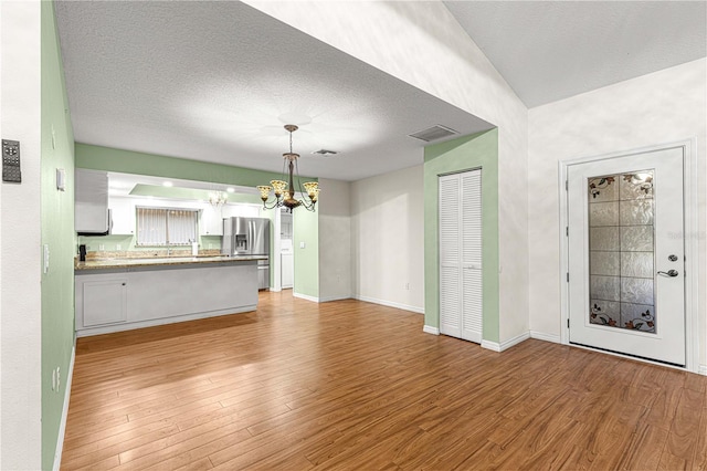 unfurnished living room featuring a textured ceiling, a notable chandelier, and light wood-type flooring