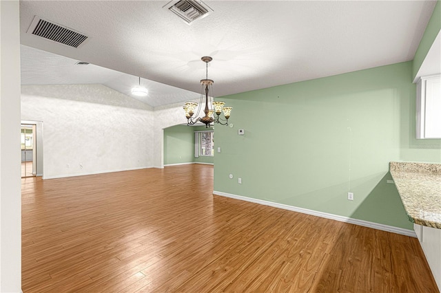 unfurnished dining area featuring hardwood / wood-style flooring, a chandelier, a textured ceiling, and vaulted ceiling