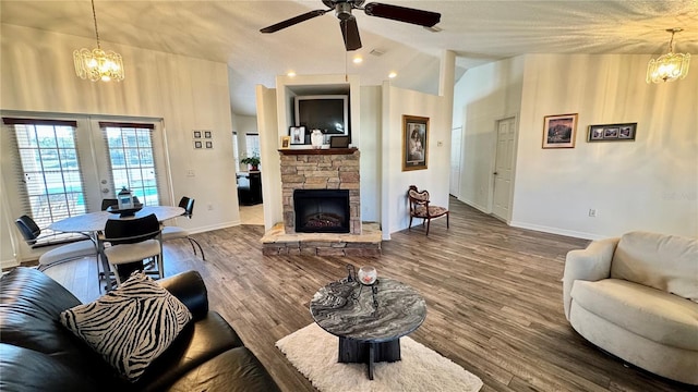 living room with hardwood / wood-style floors, lofted ceiling, french doors, ceiling fan with notable chandelier, and a stone fireplace