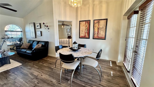 dining space with dark hardwood / wood-style floors, ceiling fan with notable chandelier, and high vaulted ceiling