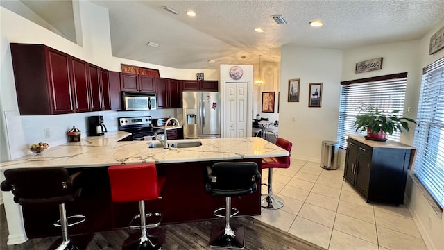 kitchen featuring sink, kitchen peninsula, a textured ceiling, a breakfast bar, and appliances with stainless steel finishes