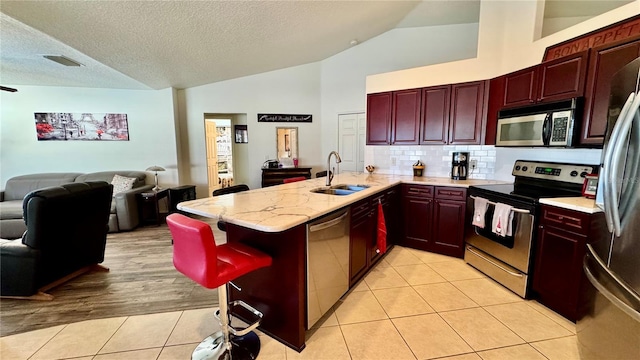 kitchen with kitchen peninsula, appliances with stainless steel finishes, vaulted ceiling, sink, and light hardwood / wood-style floors