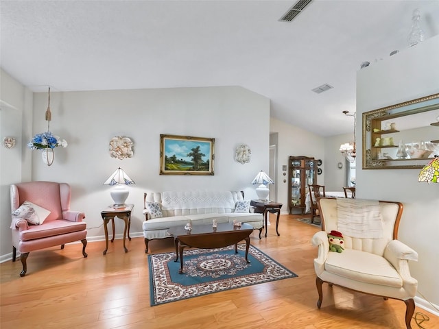 living room featuring light hardwood / wood-style floors, vaulted ceiling, and an inviting chandelier