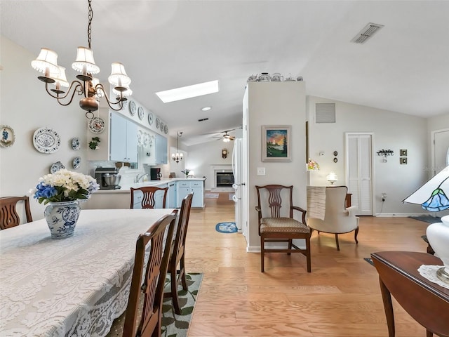 dining area featuring sink, ceiling fan with notable chandelier, light hardwood / wood-style floors, and vaulted ceiling with skylight