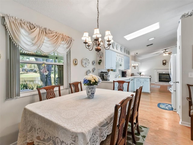 dining space featuring ceiling fan with notable chandelier, a skylight, and light hardwood / wood-style flooring