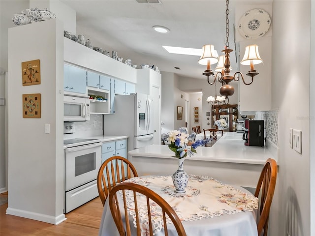 kitchen featuring a skylight, a notable chandelier, backsplash, decorative light fixtures, and white appliances