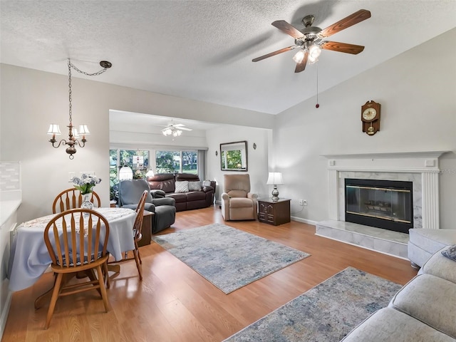 living room featuring wood-type flooring, lofted ceiling, a textured ceiling, a fireplace, and ceiling fan with notable chandelier