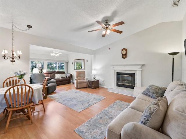 living room with a textured ceiling, light hardwood / wood-style flooring, a tile fireplace, and vaulted ceiling