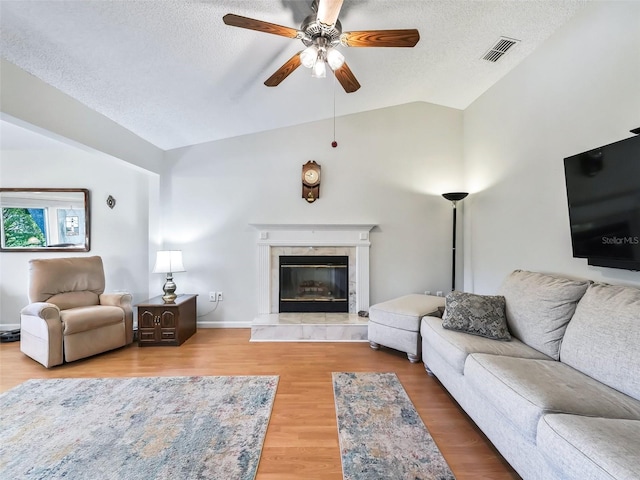 living room featuring wood-type flooring, lofted ceiling, a textured ceiling, and a tile fireplace