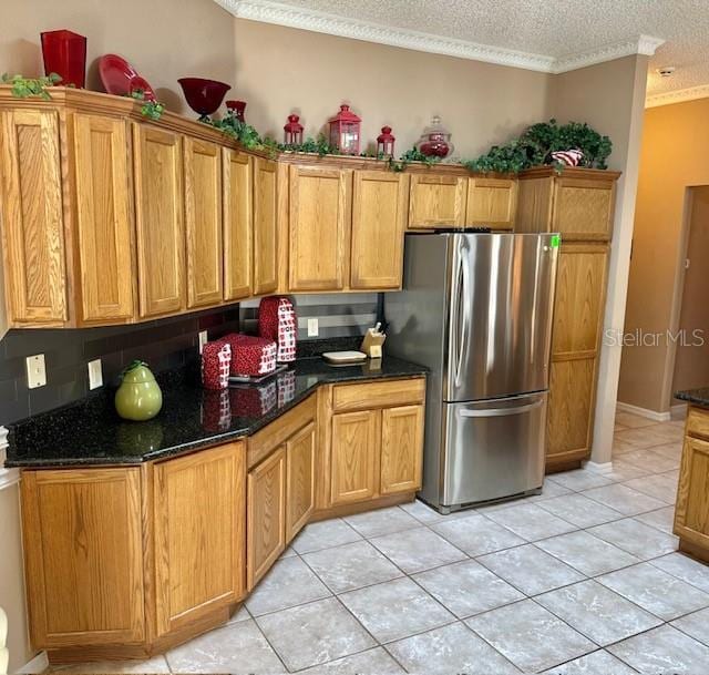 kitchen with light tile patterned flooring, dark stone countertops, a textured ceiling, and stainless steel refrigerator