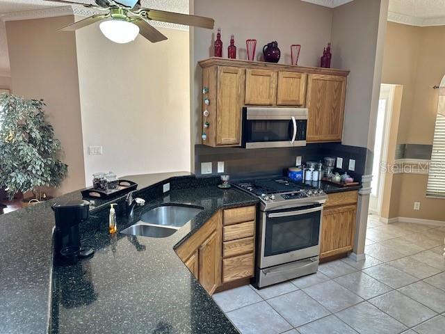 kitchen with ceiling fan, sink, stainless steel appliances, crown molding, and light tile patterned floors