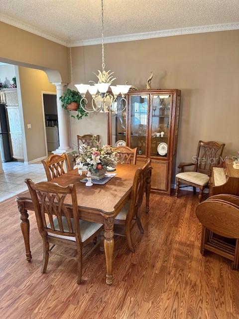 dining room with ornamental molding, a textured ceiling, a notable chandelier, wood-type flooring, and decorative columns