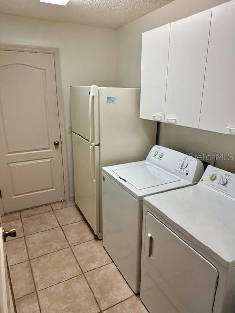 laundry area featuring cabinets, light tile patterned floors, a textured ceiling, and washing machine and clothes dryer