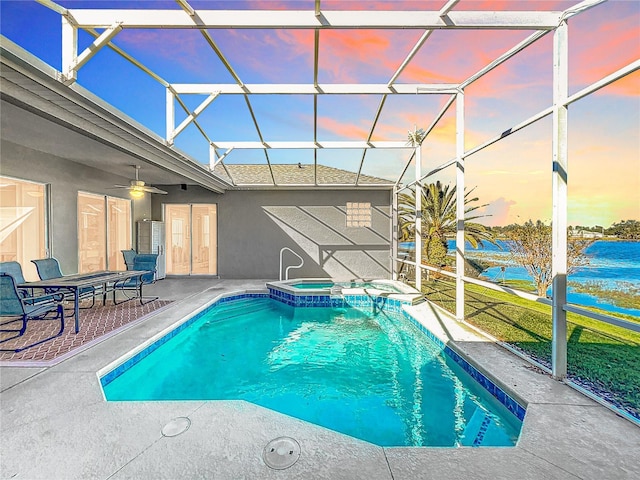 pool at dusk featuring a lanai, a patio area, ceiling fan, and an in ground hot tub