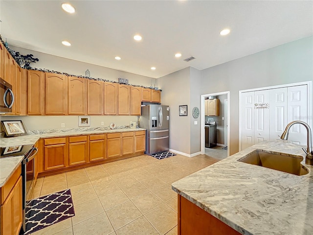 kitchen with sink, light stone counters, washer / dryer, light tile patterned floors, and appliances with stainless steel finishes