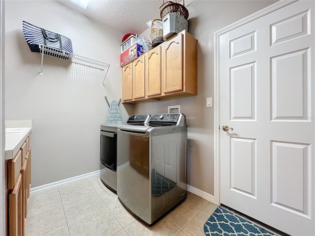 washroom featuring washing machine and clothes dryer, light tile patterned floors, cabinets, and a textured ceiling