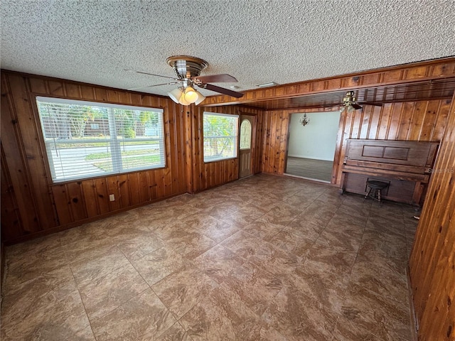 unfurnished room with wooden walls, ceiling fan, and a textured ceiling