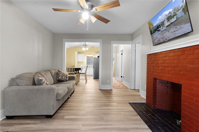 living room with ceiling fan, a brick fireplace, and light hardwood / wood-style flooring