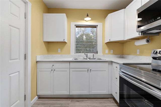 kitchen with sink, light wood-type flooring, white cabinets, and appliances with stainless steel finishes