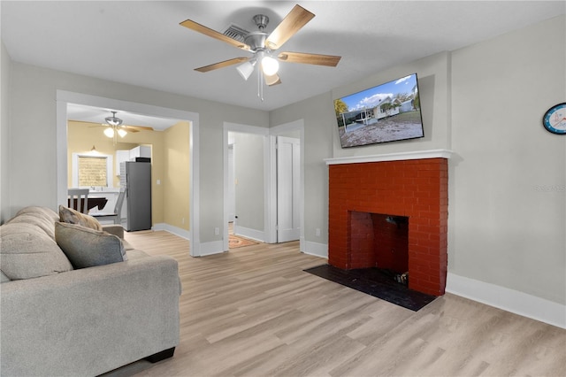 living room featuring ceiling fan, a fireplace, and light hardwood / wood-style flooring