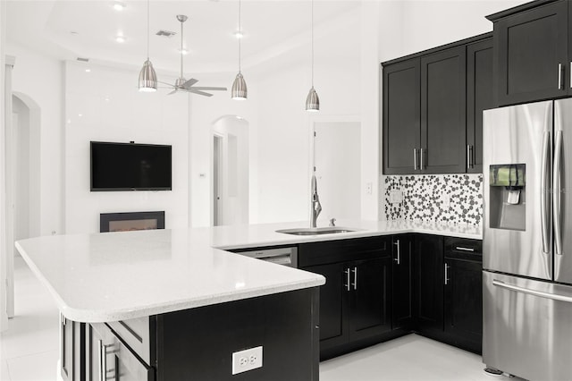 kitchen with sink, hanging light fixtures, ceiling fan, stainless steel fridge, and decorative backsplash