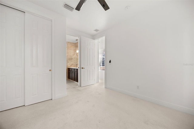 unfurnished bedroom featuring ceiling fan, a closet, ensuite bathroom, and light carpet