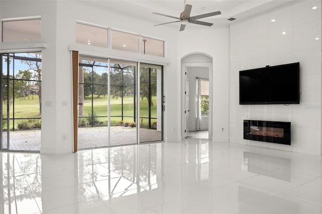 unfurnished living room with a large fireplace, ceiling fan, a healthy amount of sunlight, and tile patterned flooring