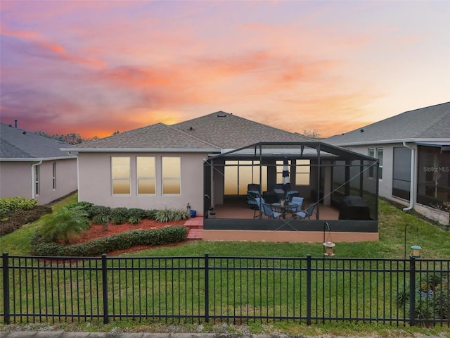 back house at dusk featuring a yard, glass enclosure, and a patio area