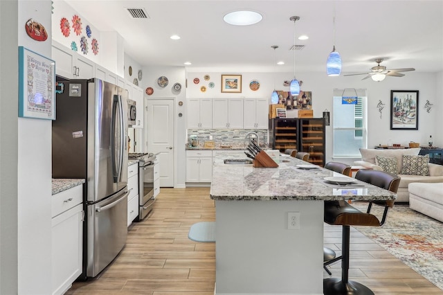 kitchen with white cabinetry, sink, hanging light fixtures, stainless steel appliances, and a kitchen breakfast bar