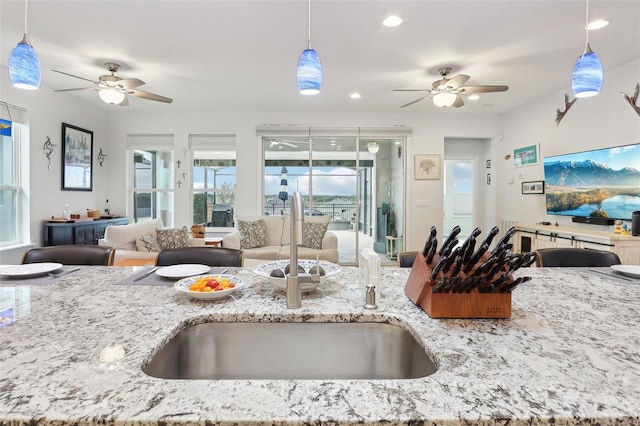 kitchen featuring light stone counters, sink, ceiling fan, and decorative light fixtures