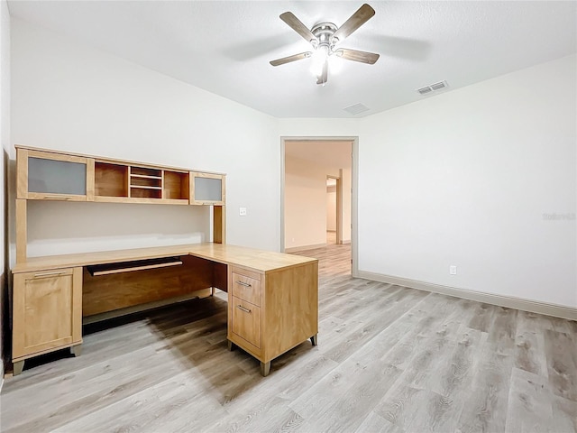 unfurnished office featuring built in desk, light hardwood / wood-style flooring, and ceiling fan