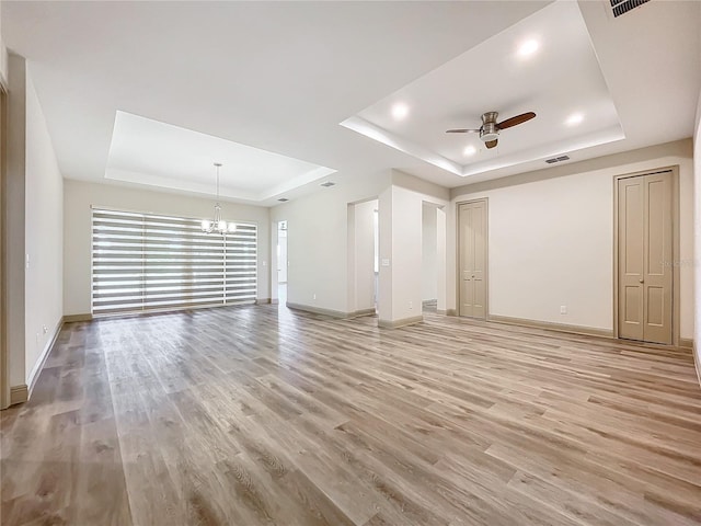 unfurnished living room with ceiling fan with notable chandelier, light hardwood / wood-style floors, and a raised ceiling