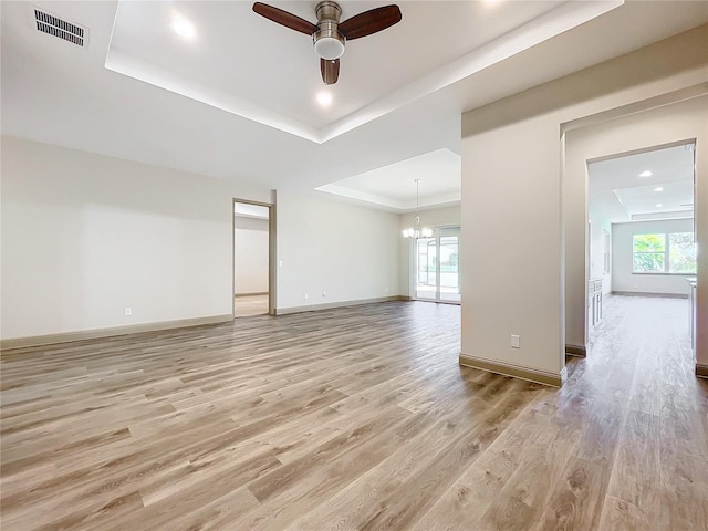 empty room with ceiling fan with notable chandelier, light hardwood / wood-style floors, and a tray ceiling