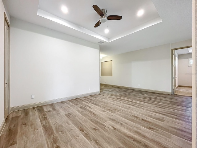 spare room with ceiling fan, light hardwood / wood-style floors, and a raised ceiling