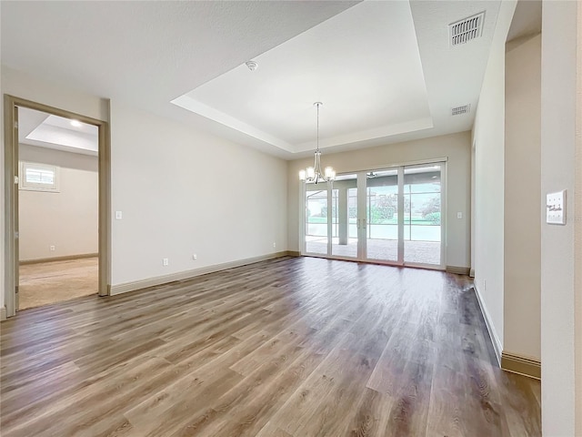 unfurnished room featuring a raised ceiling, wood-type flooring, and a chandelier