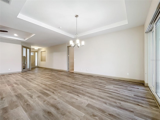 unfurnished dining area with light hardwood / wood-style floors, a raised ceiling, and an inviting chandelier