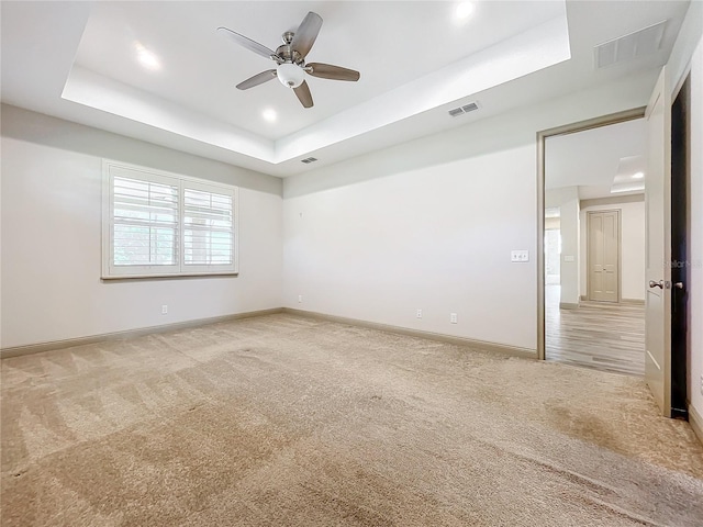 unfurnished room with a raised ceiling, light carpet, and ceiling fan