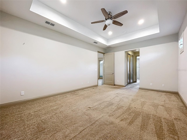 empty room with a raised ceiling, ceiling fan, and light carpet