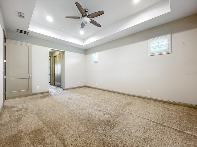 spare room with ceiling fan, a raised ceiling, and light carpet