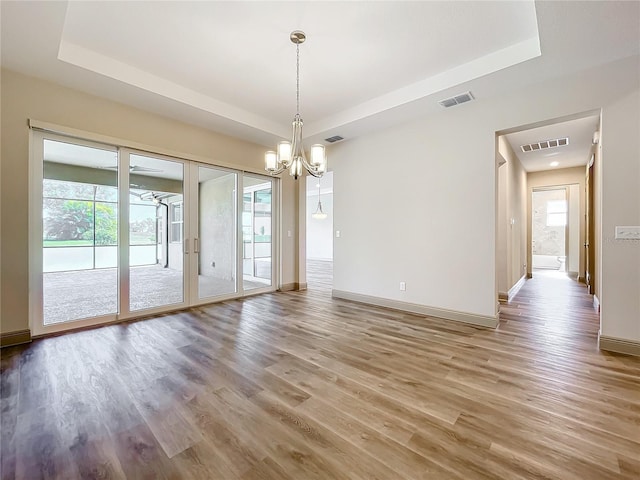 unfurnished dining area featuring hardwood / wood-style floors, a raised ceiling, and a notable chandelier